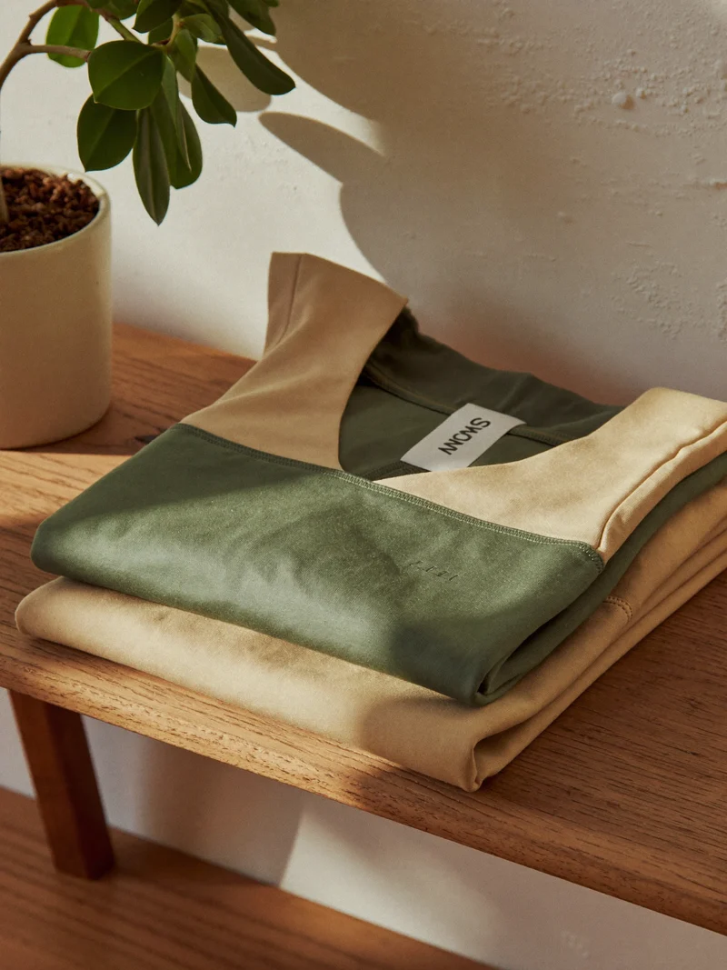 Leggings e top in cotone organico piegati sulla panca, toni salvia e sabbia